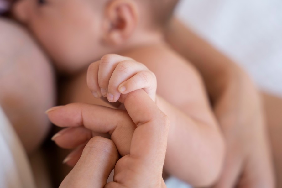 Bebê segurando a mão da mãe enquanto mama.
